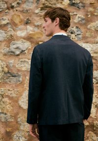 Dunkel maßgeschneiderter Blazer mit glatter Textur und strukturiertem Schnitt, ausgestattet mit einem Zwei-Knopf-Manschette und einem Schlitz hinten.