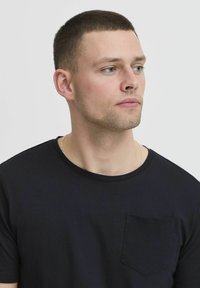 Camiseta de algodón negra de manga corta, con cuello redondo y un bolsillo en el pecho izquierdo. Textura suave con sutiles detalles de costura.