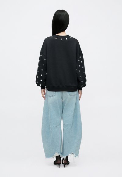 Čierna mikina s ozdobnými rukávmi, kombinovaná so svetlomodrými oversized džínsami s roztrhanými lemami. Čistý a moderný dizajn.