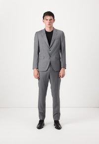 Grau Anzug mit zwei Knöpfen, mit Revers und seitlichen Taschen. Schwarzes Hemd darunter, kombiniert mit schwarzen LederSchuhen. Glatte Textur.
