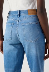 Svijetloplave traperice s visokim strukom, dva stražnja džepa i bež kožni uložak s natpisom "TOMMY JEANS" na pojasu.