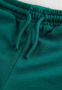 Tiinrohelised puuvillased lühikesed püksid, millel on elastne vöökoht nööriga, sile pind ja lihtne disain ilma täiendavate mustriteta.