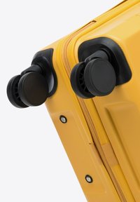 Valigia gialla rigida con superficie texturizzata, doppie ruote nere e chiusura con zip. Include dettagli neri e hardware resistente.