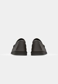 Paire de chaussures habillées en cuir noir vues du talon sur un fond blanc uni.