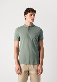 Lysegrønn polo i myk stoff, med en tre-knapps knappestolpe og brodert logo. Korte ermer med kontrasterende detalj.