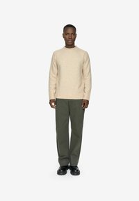 Un pull en tricot beige avec un col rond, associé à un pantalon ample vert olive et des chaussures noires. L'ensemble présente une apparence texturée.