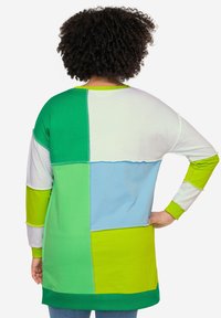 Túnica de manga larga y patchwork que presenta segmentos en verde, azul y blanco. Tejido suave con costuras en contraste y un diseño de ajuste relajado.
