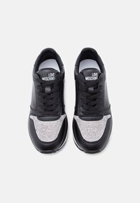 Μαύρα αθλητικά παπούτσια με λαμπερό ασημί πάνελ από στρας, υφασμένο άνω μέρος, μαύρα κορδόνια και το λογότυπο "LOVE MOSCHINO" στη γλώσσα.