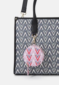 Sac fourre-tout noir à motifs avec un design en zigzag gris et blanc, doté d'une trousse ronde zippée rose et rouge attachée par un fermoir en or.