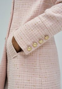 Roze tweed sako s teksturiranim uzorkom i metalnim nitima, s džepom i zlatnim dugmadima na manžetama.