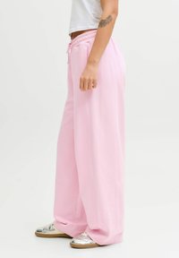 Vaaleanpunaiset leveälahkeiset collegehousut, joissa on joustava vyötärönauha ja kiristysnyöri, valmistettu pehmeästä kankaasta. Yhdistetty hopeisiin ja beigenvärisiin lenkkareihin.