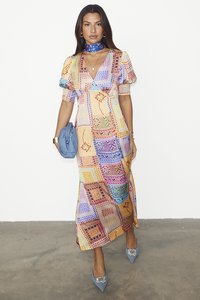 Robe maxi avec un design en patchwork coloré, manches courtes bouffantes et décolleté en V. Associée à des escarpins bleus à bouts pointus et à un sac à main bleu assorti.