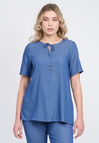 Top blu corto con maniche a sudore, scollo rotondo e dettaglio con fiocco sul davanti. Tessuto liscio con una finitura leggermente strutturata. Vestibilità ampia.