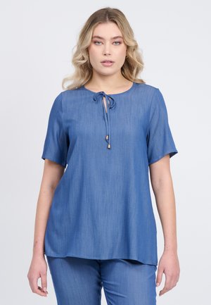 Top blu corto con maniche a sudore, scollo rotondo e dettaglio con fiocco sul davanti. Tessuto liscio con una finitura leggermente strutturata. Vestibilità ampia.