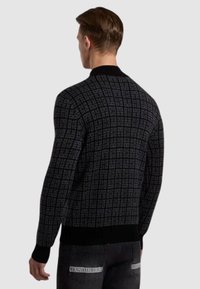 Maglione nero lavorato a maglia con motivo geometrico, colletto e polsini a costine, e design aderente. Indossato con jeans scuri.