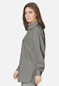 Grijze langekousen shirt met een kraag, voorzien van een zijsplit, knoopsluiting en een gladde textuur. Het ontwerp heeft een relaxte pasvorm en minimalistische details.