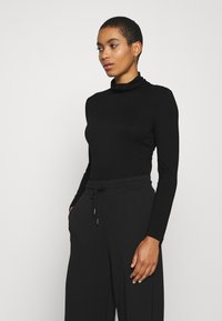 Black long-sleeve turtleneck top with a fitted design, paired with loose black pants featuring an elastic waistband and side pockets.