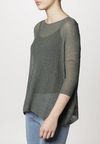 Suéter gris de punto con un corte holgado, mangas tres cuartos y un diseño texturizado. Combinado con jeans de mezclilla azul claro.