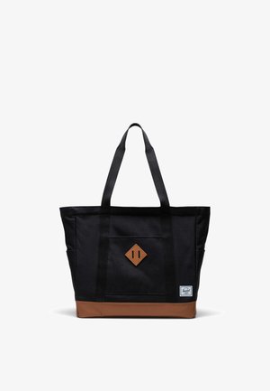 Bolsa de tela negra con acento en la parte inferior marrón, que cuenta con dos asas resistentes y un parche de cuero en forma de diamante en la parte frontal.