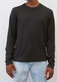 Schwarzer langärmliger Rundhalsausschnitt-Pullover aus glattem Stoff, mit schlankem Schnitt und geripptem Kragen, kombiniert mit hellblauen Jeans.