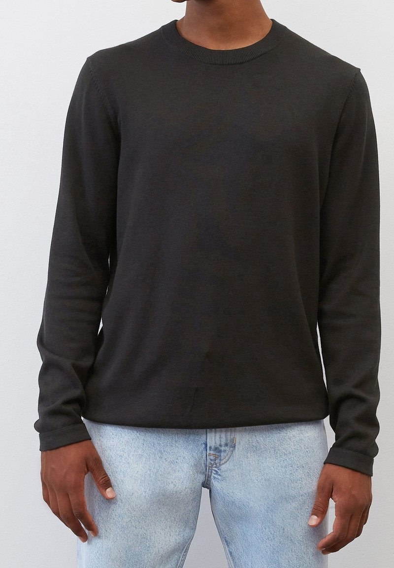 Schwarzer langärmliger Rundhalsausschnitt-Pullover aus glattem Stoff, mit schlankem Schnitt und geripptem Kragen, kombiniert mit hellblauen Jeans.