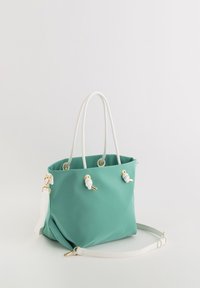 Mintgrøn tote taske lavet af holdbart materiale med hvide rebhåndtag, guldfarvede metaldele og en aftagelig hvid skulderrem.