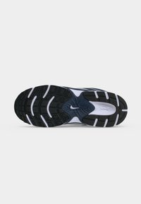 Μαύρη και λευκή σόλα αθλητικού παπουτσιού Nike με υφή και κεντρικό λογότυπο Nike swoosh σε απλό φόντο.