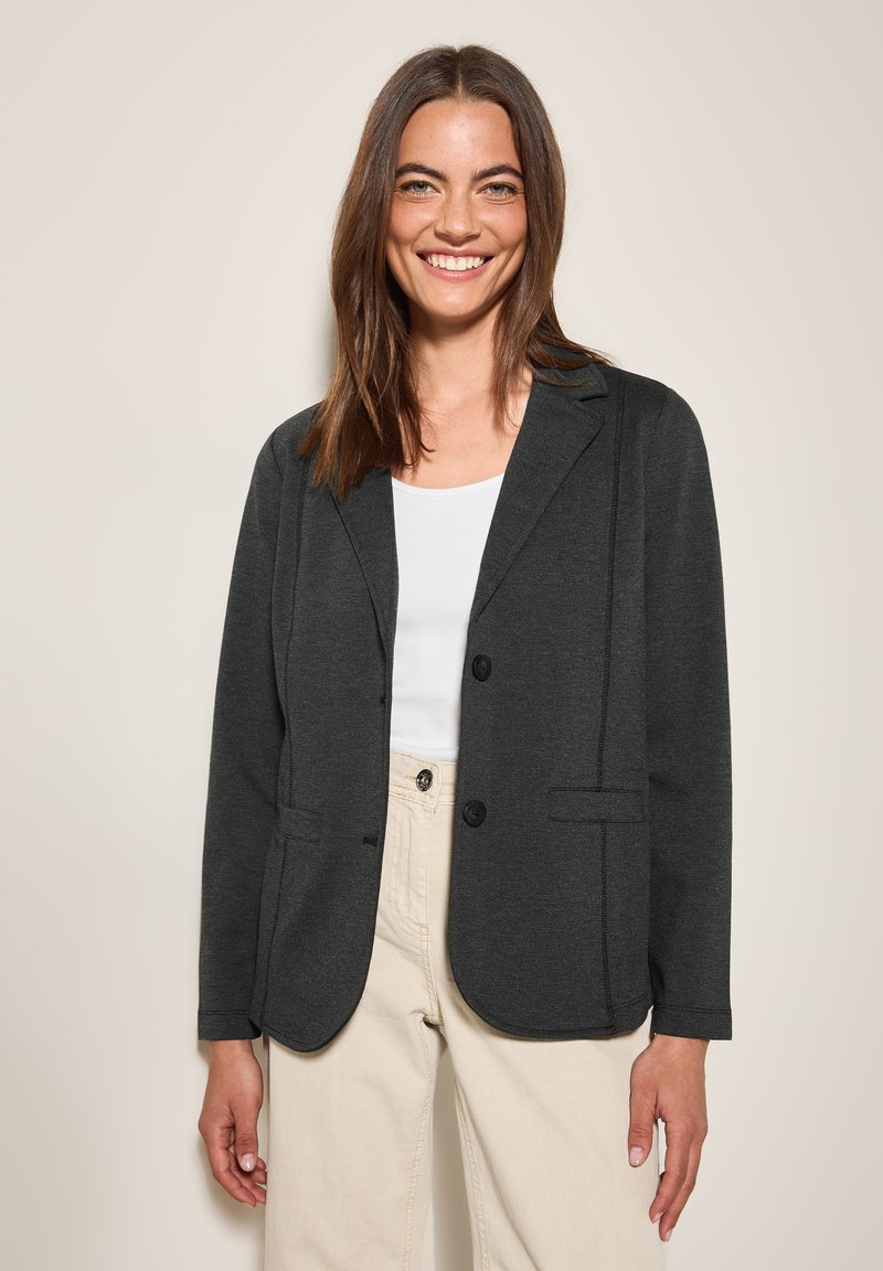 Blazer en charbon avec une coupe ajustée, doté de revers crantés, de deux poches avant et d'une fermeture à boutons, porté sur un haut blanc.