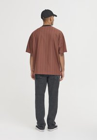 Camiseta oversized a rayas marrón con cuello redondo negro, combinada con jeans gris oscuro y zapatillas negras. La gorra también es negra.