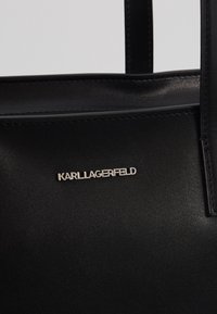 Black synthetic handbag featuring smooth texture, minimalistic design, and a silver "KARL LAGERFELD" logo accent on the front.