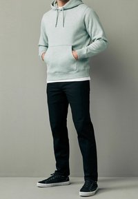 Lichtgroene hoodie met kangoeroezak en trekkoord, gecombineerd met een zwarte broek en zwarte sneakers met witte zolen.
