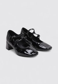 Chaussures Mary Jane en cuir verni noir avec un bout arrondi, deux brides réglables et un petit talon block. Surface lisse avec une finition brillante.