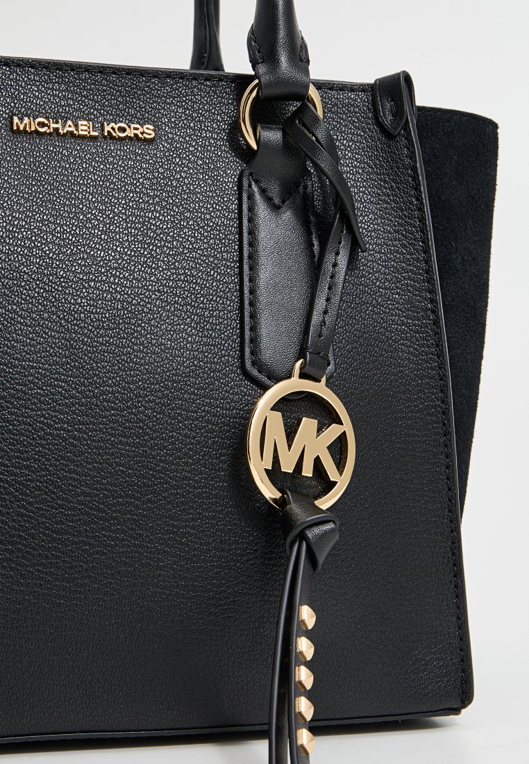 Borsa a mano in pelle nera con superficie testurizzata, caratterizzata da un charm con logo MK dorato e dettagli borchiati su una tracolla. La silhouette è strutturata.