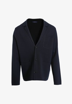 Gilet bleu marine avec un col châle, une poche poitrine et deux poches avant. Dispose d'une fermeture par boutons et d'une texture tricot douce.