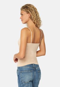 Beige linne med tunna straps, kroppsnära design, tillverkat av slät tyg. Ovanpå blå denimjeans med bakfickor.