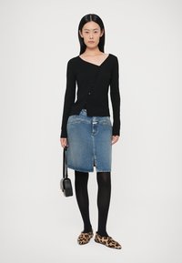 Black ribbed long-sleeve cardigan, denim skirt with front slit, black tights, leopard print loafers, and a small black shoulder bag.