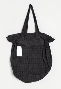 Zwarte gewatteerde schoudertas met lange handvatten en een witte rechthoekige label eraan bevestigd, weergegeven tegen een witte achtergrond.