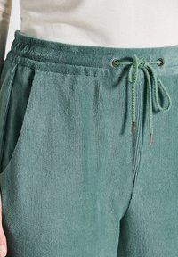 Groene corduroy broek met een elastische tailleband, trekkoorddetails, zijzakken en een gestructureerde stofafwerking.