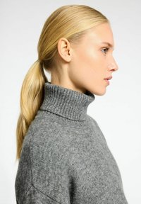 Chandail en maille gris à col roulé avec un col et un ourlet côtelés, mettant en avant une texture douce et une silhouette décontractée.