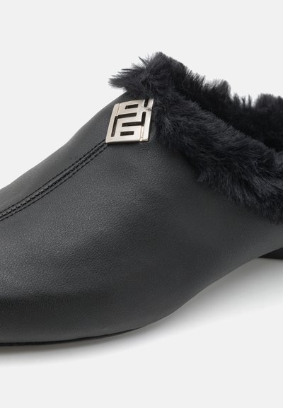 Chaussure slip-on en cuir noir avec un doublage en fourrure noire douce et un accent de logo argenté sur le côté. Texture lisse et forme arrondie.