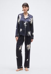 Ensemble de pyjama en satin bleu marine avec imprimé floral, haut à manches longues avec poche, et pantalon assorti à taille élastique et bordure blanche contrastante.