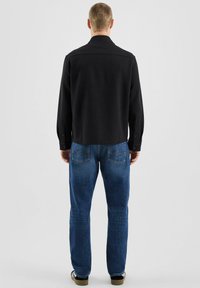 Czarna koszula z długim rękawem i kołnierzykiem, połączona z niebieskimi dżinsami. Koszula ma zapinane na guziki mankiety i dopasowany krój.