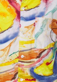 Cămașă scurtă multicolorată cu un design abstract în nuanțe de galben, albastru și portocaliu; include nasturi albi și un buzunar pe pieptul stâng.