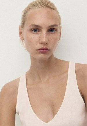 Svijetloružičasta majica na bretele s dubokim V-izrezom i tankim naramenicama. Glatka tekstura s vidljivom pjegavom kožom i plavim očima u portretu.