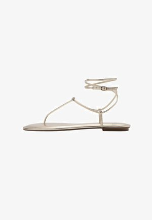 Flat metallic gold sandal with thin straps, ankle buckle, and a T-strap design on a white background.