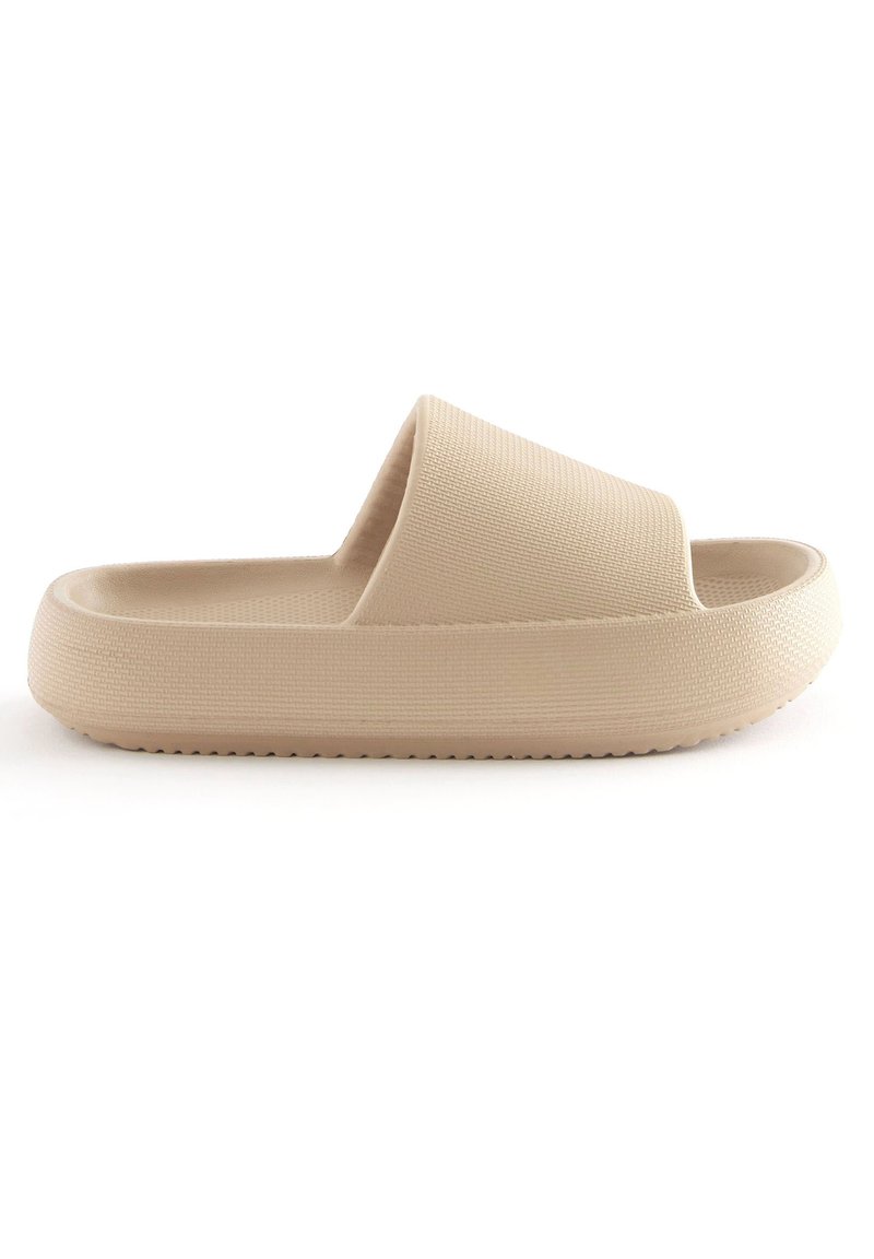 Beige slip-on sandal med en tekstureret overflade, bred rem og en tykkestøbt sål med små skridsikre dupper på bunden.