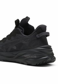 Chaussure de sport noire avec un dessus texturé, un talon renforcé et une semelle rembourrée, arborant un logo distinctif sur le côté.