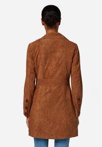 Bruine suède trenchcoat, op maat gemaakt, met een tailleband, lange mouwen met knopen aan de manchetten, soepele textuur, minimalistisch ontwerp.