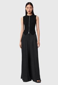 Sort ribbet top uden ærmer med lynlås foran og høj krave, kombineret med brede sorte bukser med læg og en løs pasform.