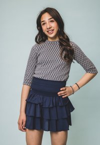 Patroon top met driekwartmouwen, gecombineerd met een marineblauwe gelaagde rok met ruches. De top heeft een geometrisch ontwerp en een smocktail.